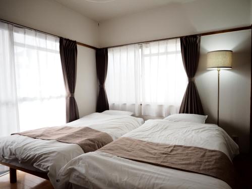 two beds in a bedroom with windows and a lamp at Living CUBE Beppu Station / Vacation STAY 54926 in Beppu