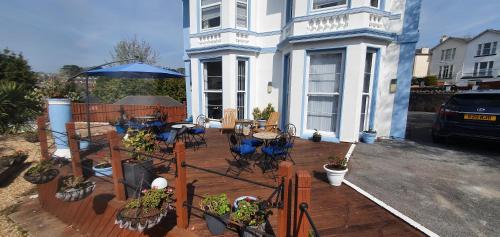 a house with a deck with tables and chairs and an umbrella at Tor Dean Guest House in Torquay