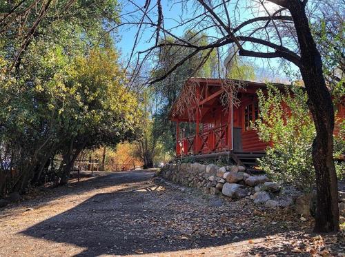 a red cabin with a stone wall next to a tree at Rancho el Chilcal Cabañas con vista al rio in San Alfonso