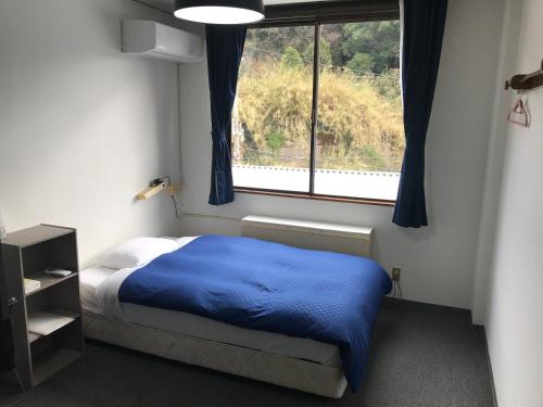 a bedroom with a bed with a blue blanket and a window at Biz Hotel Kiiyura in Yura