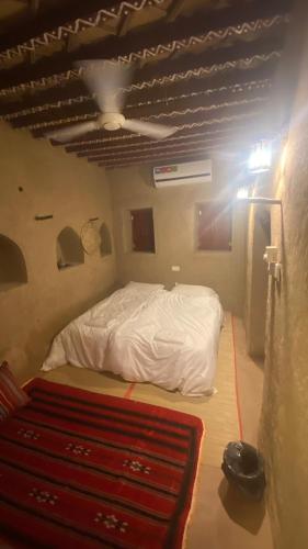 a bedroom with a white bed and a red rug at Alqalah Inn in Al Ḩamrāʼ