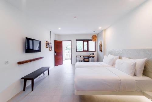 a white bedroom with a large bed and a bench at El Tropico Boutique Hotel in Kuta Lombok