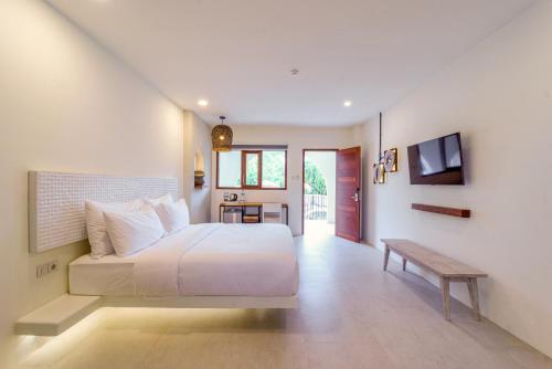 a bedroom with a large white bed and a bench at El Tropico Boutique Hotel in Kuta Lombok