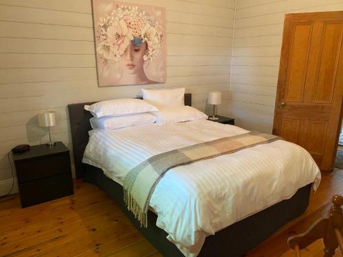 1 dormitorio con 1 cama con sábanas blancas y una pintura en DELIGHTFUL AND CHARMING ROSE COTTAGE en Kilmore