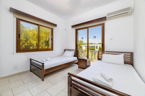 two beds in a room with two windows at Villa Sam in Ayia Napa