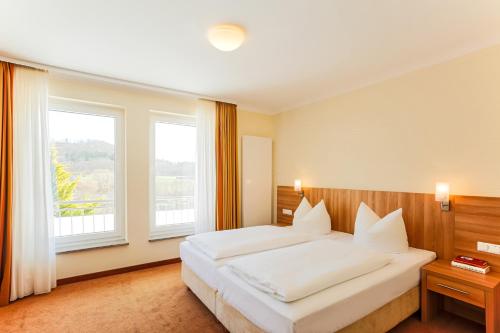 a bedroom with a large white bed and two windows at Berggasthof Banzer Wald in Bad Staffelstein