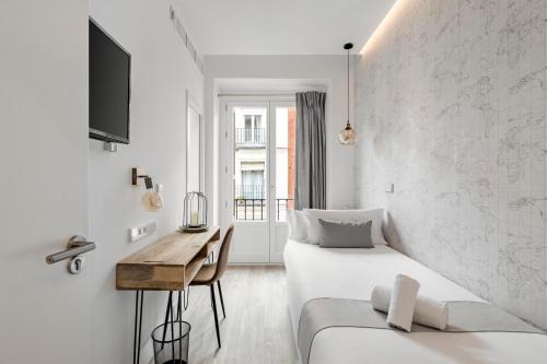 Cette chambre blanche dispose d'un lit, d'un bureau et d'une fenêtre. dans l'établissement Marco Polo Residence Hostal Boutique, à Madrid