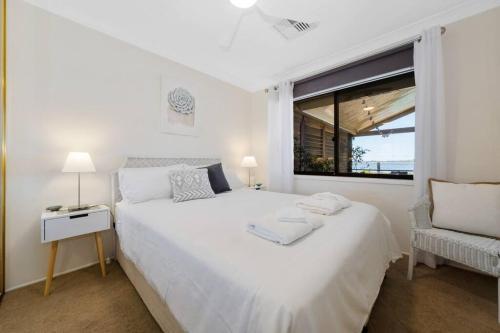 a white bedroom with a large white bed and a window at The Lake House - Luxury home with Pool in Berkeley Vale