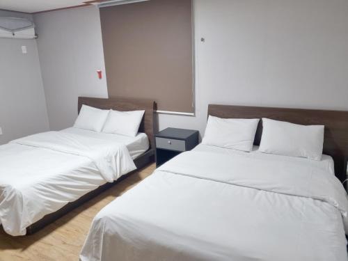 two beds in a room with white sheets and pillows at Charlie Hotel Jeju in Jeju