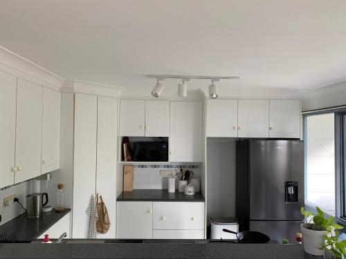 a kitchen with white cabinets and a stainless steel refrigerator at The Beachcomber in Sanctuary Point