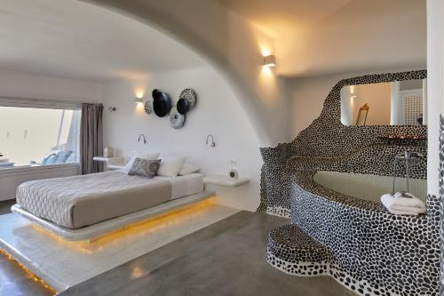 a bedroom with a bed and a mirror and a tub at Suites of the Gods Cave Spa Hotel in Megalochori