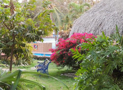 a garden with a bench and flowers and a thatch roof at Portoazul Casa de Playa in Puerto Colombia