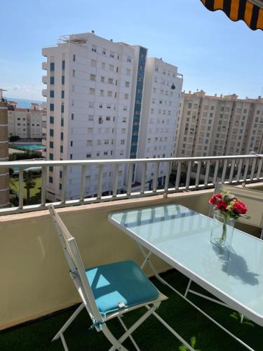 uma mesa de vidro e cadeiras numa varanda com edifícios em Apartamento La Pobla de Farnals em Valência