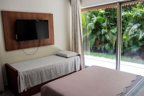um quarto com duas camas e uma televisão e uma janela em Qavi - Flat completo com vista para o jardim #ÎledePipa em Pipa