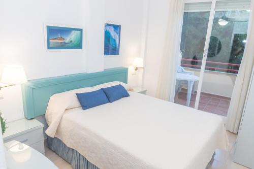 a bedroom with a bed with blue pillows and a window at Apartamento Sereno 2 - Piscina, Garaje, Terraza y Playa in Los Caños de Meca