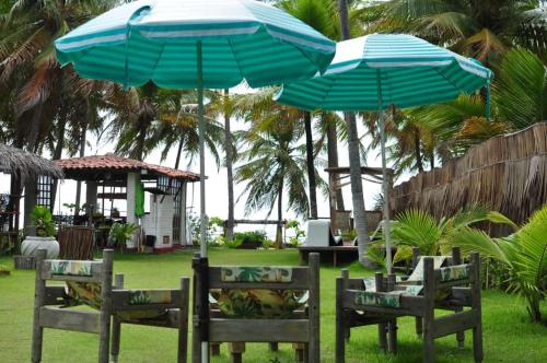 two blue umbrellas over chairs and tables in a yard at Parador Algaroba in Japaratinga