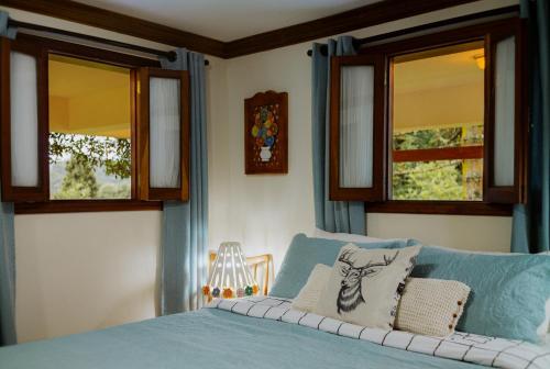 a bedroom with a blue bed and two windows at Cabana Mimosa in Monte Verde