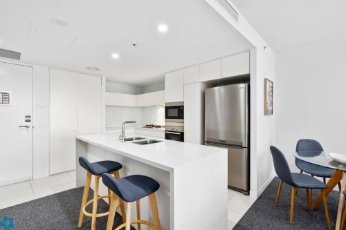 a kitchen with white cabinets and blue stools at Oracle Resort Broadbeach - gclr in Gold Coast