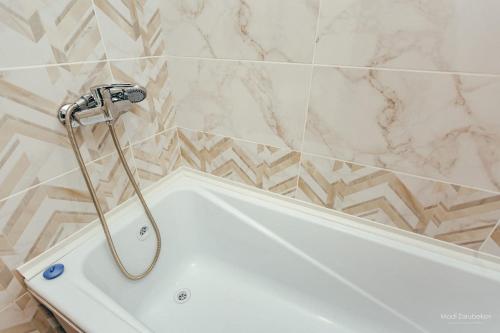 y baño con bañera blanca y azulejos de mármol. en Уютная квартира, en Semey