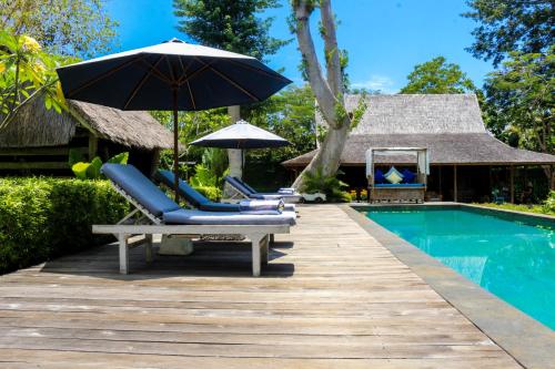 una terraza con sillas y una sombrilla junto a la piscina en Chanteak Bali - Stone House 2, en Jimbaran