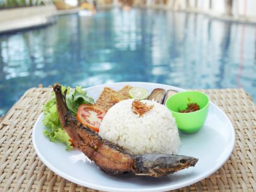 a plate of food with rice and meat next to a pool at Singaraja Hotel - CHSE Certified in Singaraja