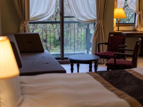 a hotel room with a bed and a chair and a window at 伊豆高原温泉ホテル 森の泉 in Ito