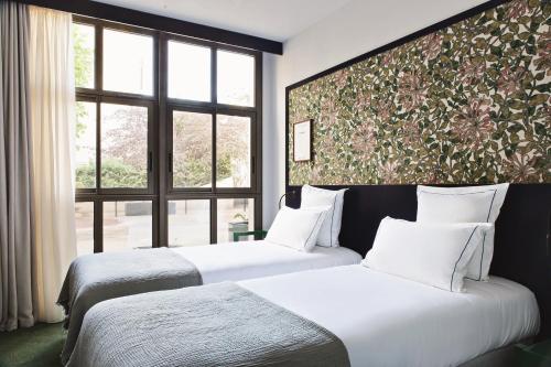 two beds in a hotel room with a large window at Hôtel Rosalie in Paris