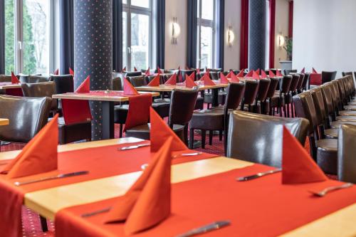 a row of tables and chairs in a room with red tables at Hotel Belmondo Leipzig Airport in Wiedemar
