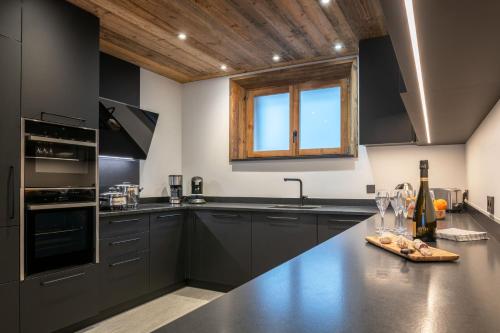 a kitchen with black cabinets and a wooden ceiling at Le refuge des Sens Chalet Harmonie in Vaujany