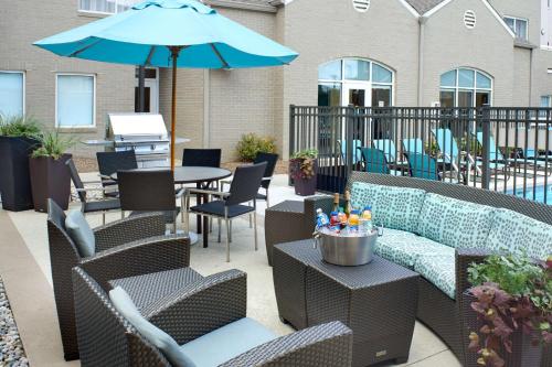 eine Terrasse mit Stühlen und einem Tisch mit einem Sonnenschirm in der Unterkunft Sonesta ES Suites Detroit Warren in Warren