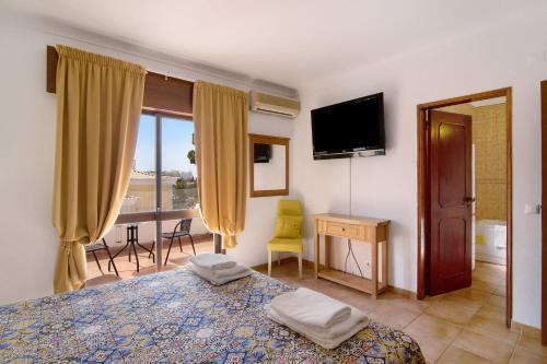 een slaapkamer met een bed, een bureau en een televisie bij Villa Fernando in Quarteira