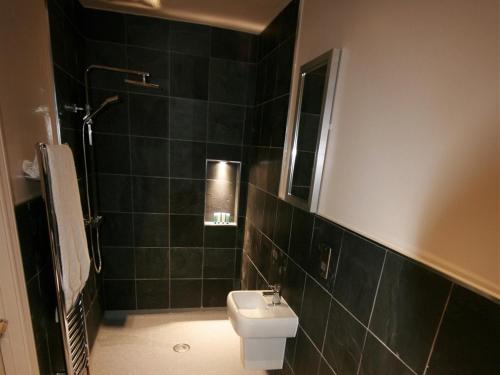 Baño de azulejos negros con aseo y lavamanos en Colchester Boutique Hotel en Colchester