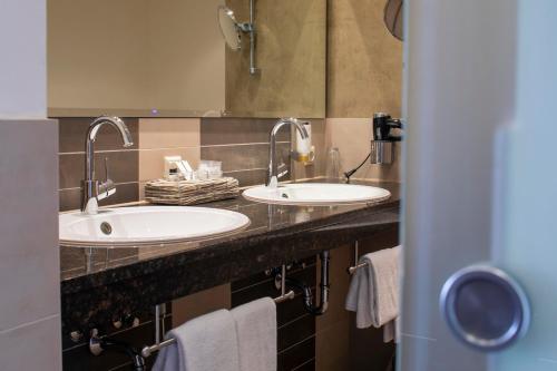 two sinks in a bathroom with two mirrors and towels at Hotel Landhaus Pollmeyer in Friesoythe