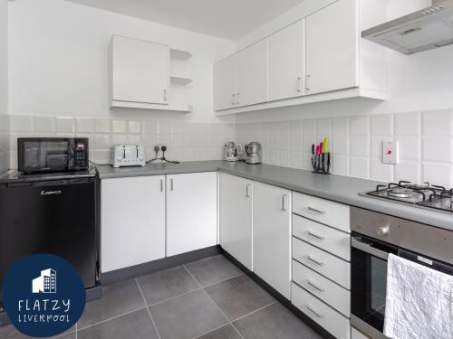 リバプールにあるFLATZY - Quiet Sefton Park Luxury Apartmentの白いキャビネットと黒の電化製品が備わるキッチン