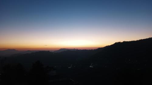 a sunset over a mountain range with the sun setting at Thakur homes- couple and family friendly homestay in Shimla