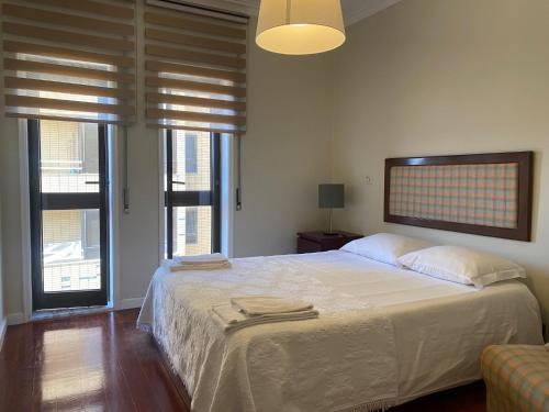 a bedroom with a bed with white sheets and windows at Apartamento Ruy Belo - Foz in Vila do Conde