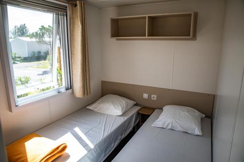 two beds in a small room with a window at amorosa mobil home in Canet-en-Roussillon