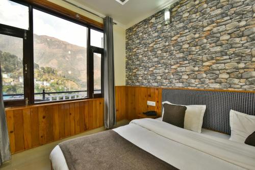 1 dormitorio con 1 cama grande y pared de piedra en The Posh Hotel, en McLeod Ganj