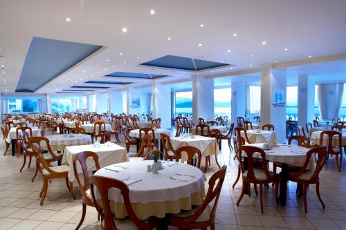a restaurant with white tables and chairs and windows at Sunshine Corfu Hotel And Spa in Nisakion