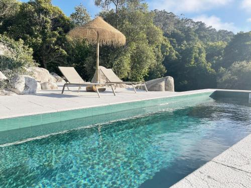 a pool with two chairs and an umbrella and water at Eighteen21 Houses - Quinta Velha in Sintra