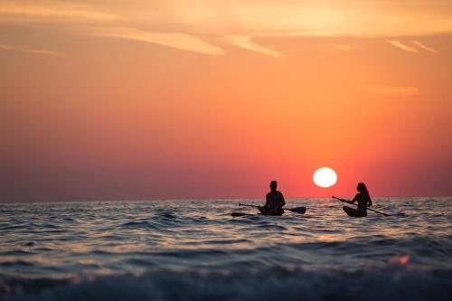 two people sitting on kayaks in the ocean at sunset at Baga Fantacia Beach Inn in Baga