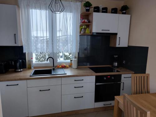 een keuken met witte kasten, een wastafel en een raam bij Uroczy Domek z Kominkiem in Lipowa