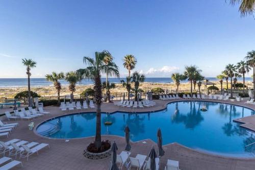 einen Pool mit Stühlen, Palmen und Strand in der Unterkunft Bristol 109 - Lovely Ground Floor Beachfront Unit in Gulf Shores