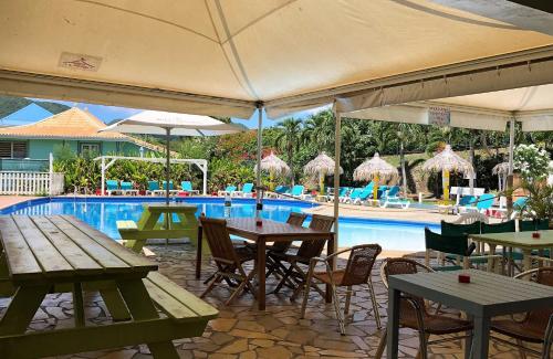un patio esterno con tavoli, sedie e piscina di Le Mayann a Le Diamant