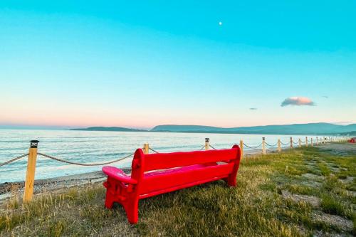 a red bench sitting on the grass near the ocean at Glenghorm Beach Resort in Ingonish