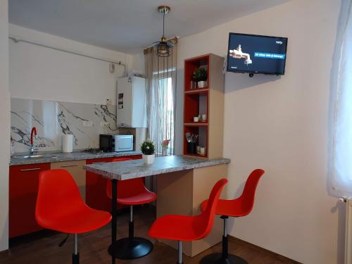 a kitchen with red chairs and a table with a tv on the wall at GARSONIERA DANIA&PETRU in Tîrgu Ocna