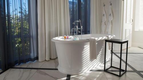 a white bath tub in a bathroom with a window at The Manor House at the Queen Victoria Hotel by NEWMARK in Cape Town