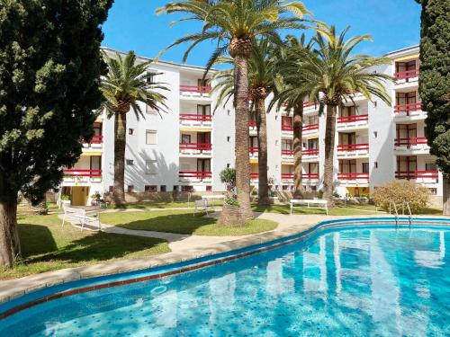 a swimming pool with palm trees in front of a building at Apartamentos Córcega Palmyra in Salou