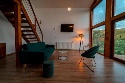 a living room with a staircase and a green chair at Le Chalet M - Cabană cu o panoramă de poveste. in Şurdeşti