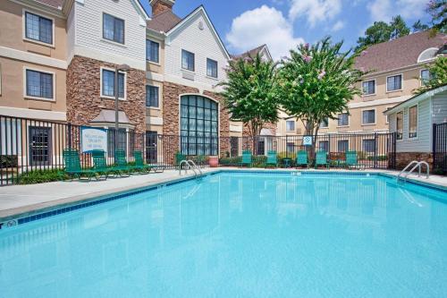 a swimming pool with chairs and trees in front of a building at Sonesta ES Suites Atlanta Alpharetta Avalon in Alpharetta